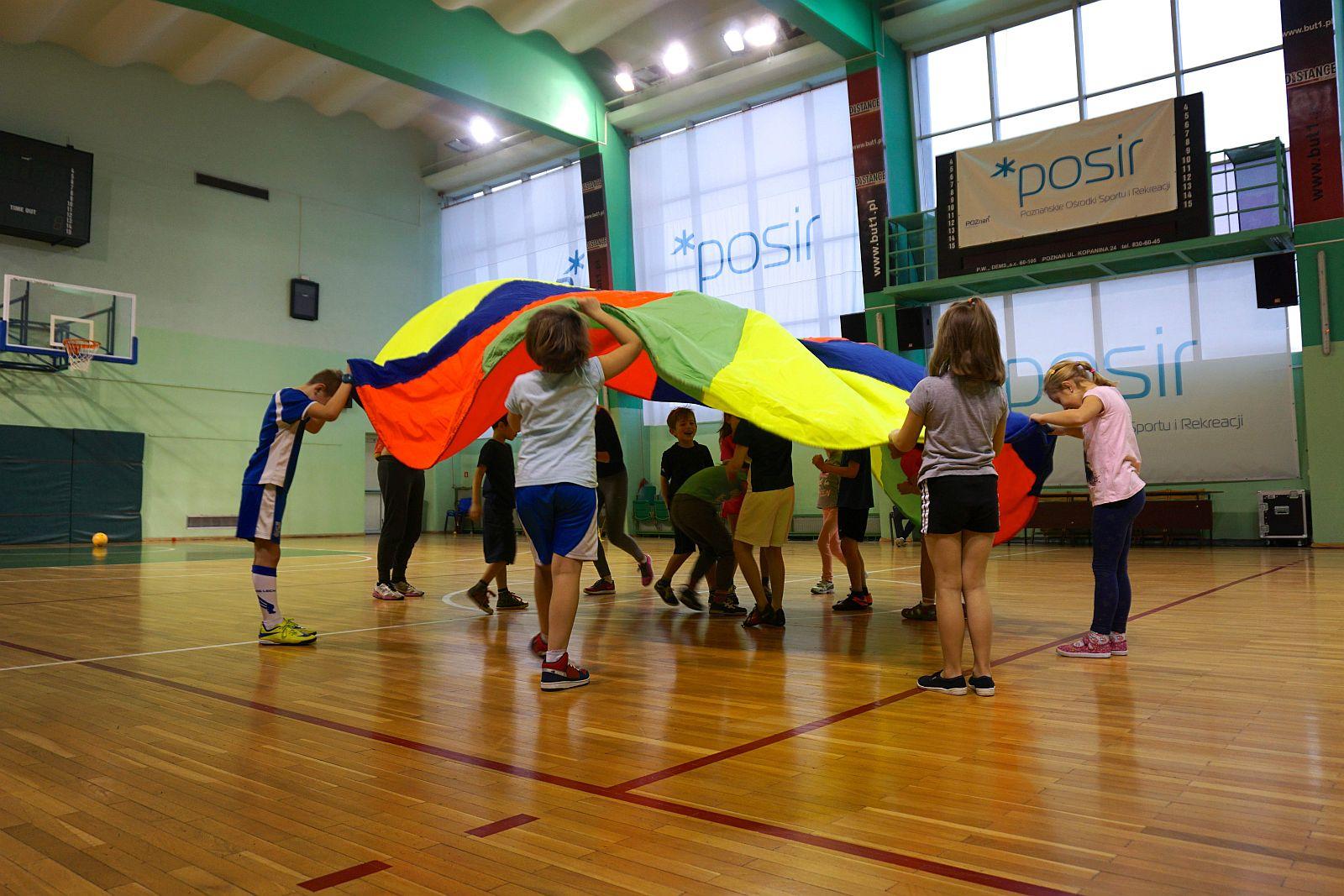 Dzieci bawią się kolorową chustą na hali sportowej